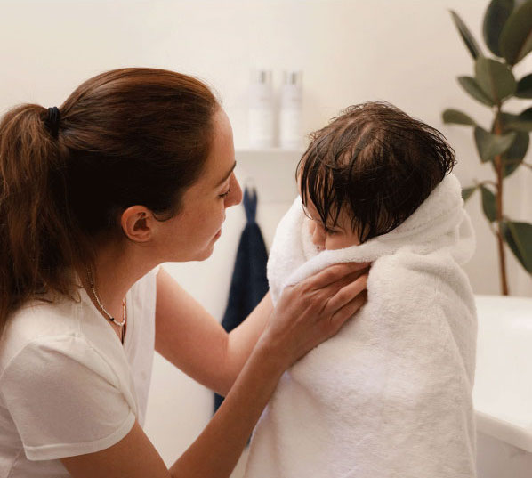 Mom drying off child with a towel after showering.