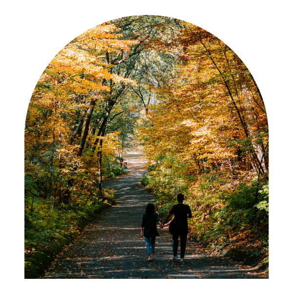 Image of mother and daughter walking down a paved trail through the woods during autumn.