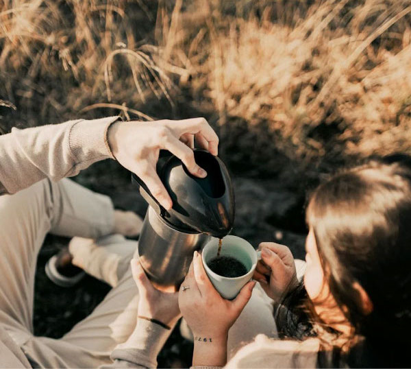 Couple pouring coffee in a meadow during an autumn morning.