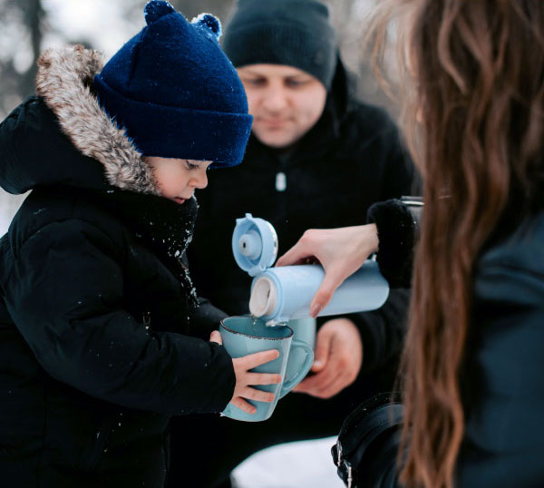 Image of mother pouring hot fresh water into child's mug in the outdoor winter.