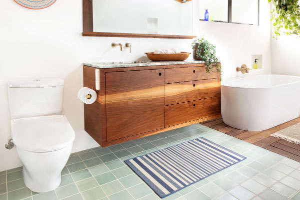 A sleek bathroom features the white 'Thinline' toilet seat, wooden shelves with towels and toiletries, a white cabinet, and a framed abstract painting on the wall.