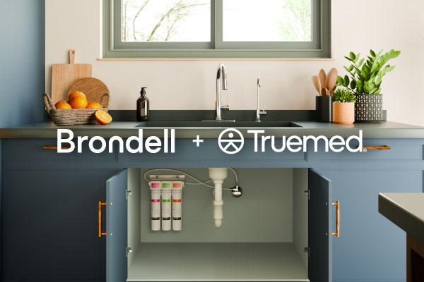 Kitchen sink with open cabinet showing an under-sink water filtration system, with the Brondell + Trumed logos overlaid on the image.