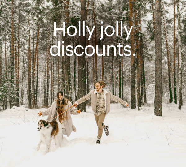 Couple walking through a snowy forest with their dog, bundled in winter clothing and smiling as they enjoy the fresh snow, with tall pine trees creating a festive, wintry backdrop