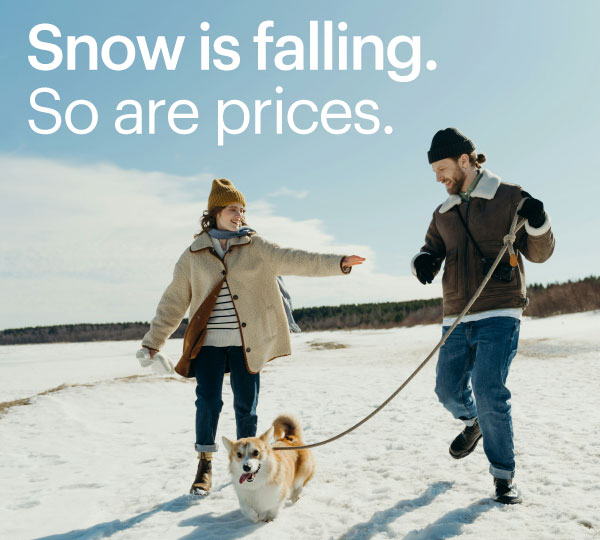 Couple walking their dog across a snowy landscape under a bright winter sky, laughing and bundled in warm clothing as the energetic dog leads the way across the open, snow-covered field.