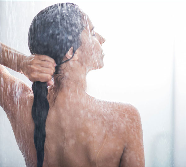 Woman enjoying a refreshing shower, water cascading over her shoulders as she gathers her wet hair, highlighting a clean spa-like experience with an eco-friendly shower system