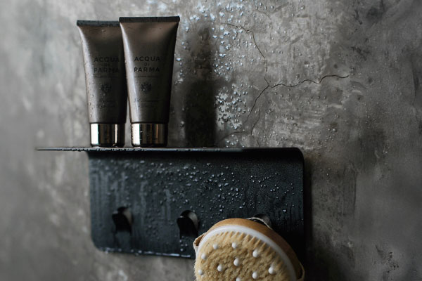 Nebia Shower Shelf in matte black mounted on a tiled wall, holding shower essentials with integrated hooks below for hanging bath accessories.