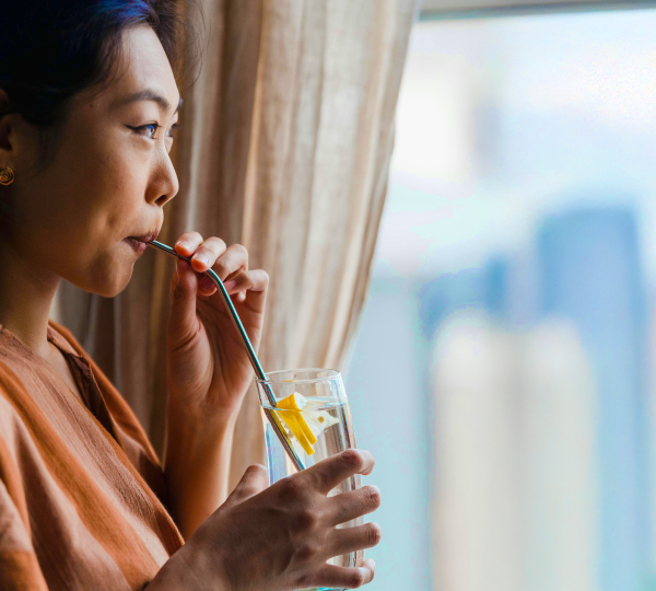 Woman drinking a glass of clean water by a window, representing fresh filtered water at home. Save 20% on under sink water filtration systems during our limited-time sale.