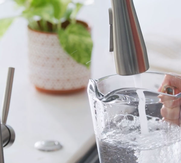 Close-up of a kitchen faucet filling a clear glass with fresh water. Crisp, clean stream highlights refreshing hydration and everyday use in a bright, modern kitchen.