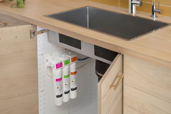 Coral Three-Stage Under Sink Water Filtration System installed beneath a modern kitchen sink, featuring compact filters that deliver clean, great-tasting filtered water while maximizing cabinet space.